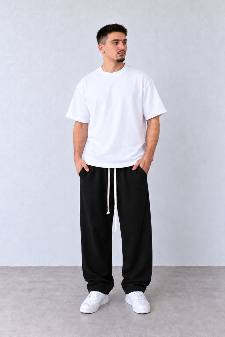 Croială lejeră și șnururi lungi la pantalonii baggy negri pentru bărbați, pe model în poziție alternativă.