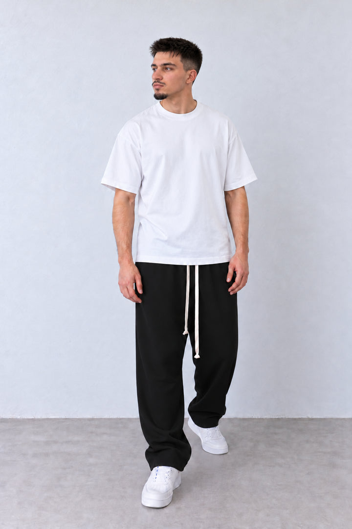 Pantaloni negri cu talie elastică, croială baggy și tiv drept, pe model în postură relaxată.