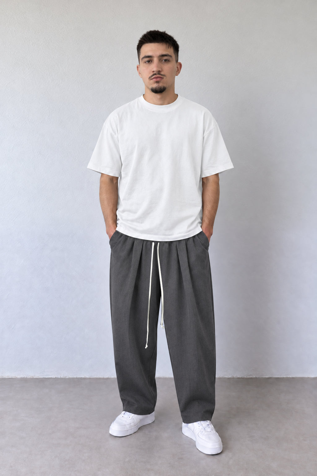 Pantaloni gri pentru bărbați cu pense și șnur lung, purtați cu tricou alb, vedere integrală.