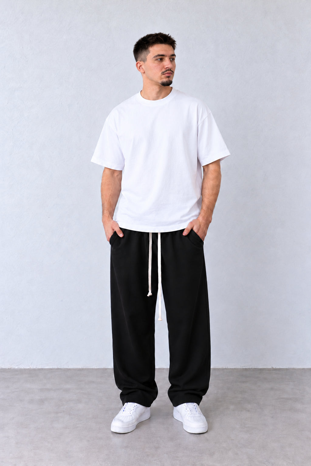 Croială lejeră și șnururi lungi la pantalonii baggy negri pentru bărbați, pe model în poziție alternativă.