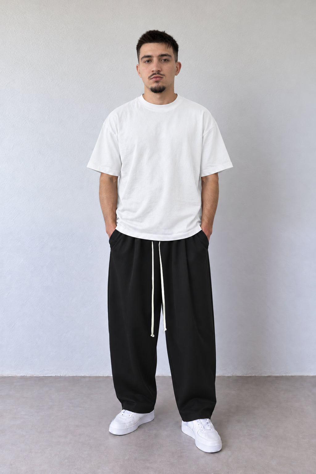 Pantaloni negri pentru bărbați cu șnur alb lung, purtați cu tricou alb, vedere integrală.