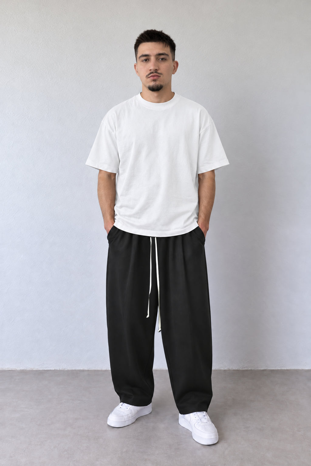 Pantaloni negri baggy pentru bărbați, cu șnur alb lung, purtați cu tricou alb, vedere integrală.