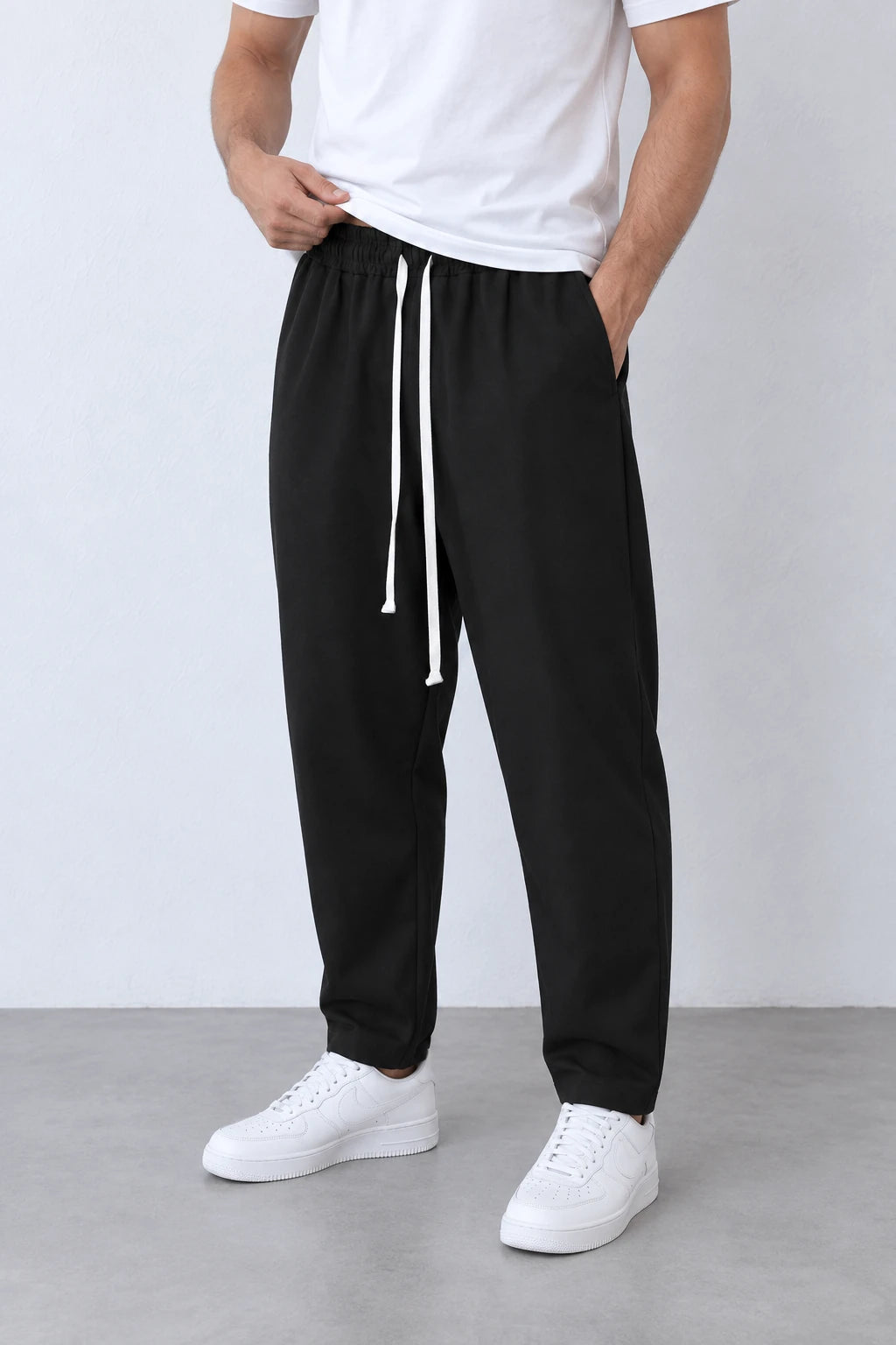 Pantaloni lungi negri carrot fit pentru bărbați, vedere din trei sferturi a croielii și a șnurului alb lung.
