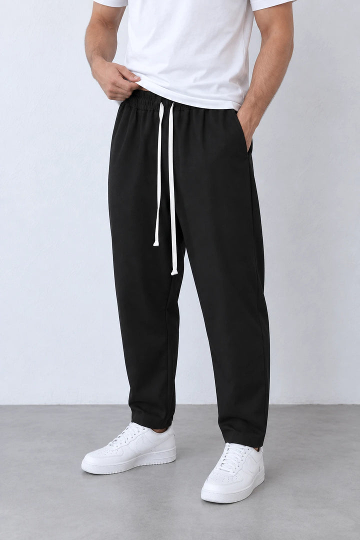 Pantaloni lungi negri carrot fit pentru bărbați, vedere din trei sferturi a croielii și a șnurului alb lung.