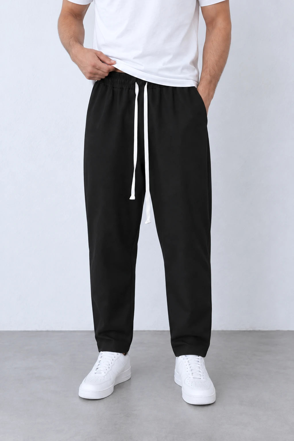 Pantaloni negri ușor slim cu talie elastică și două capete de șnur alb lung, vedere frontală apropiată.