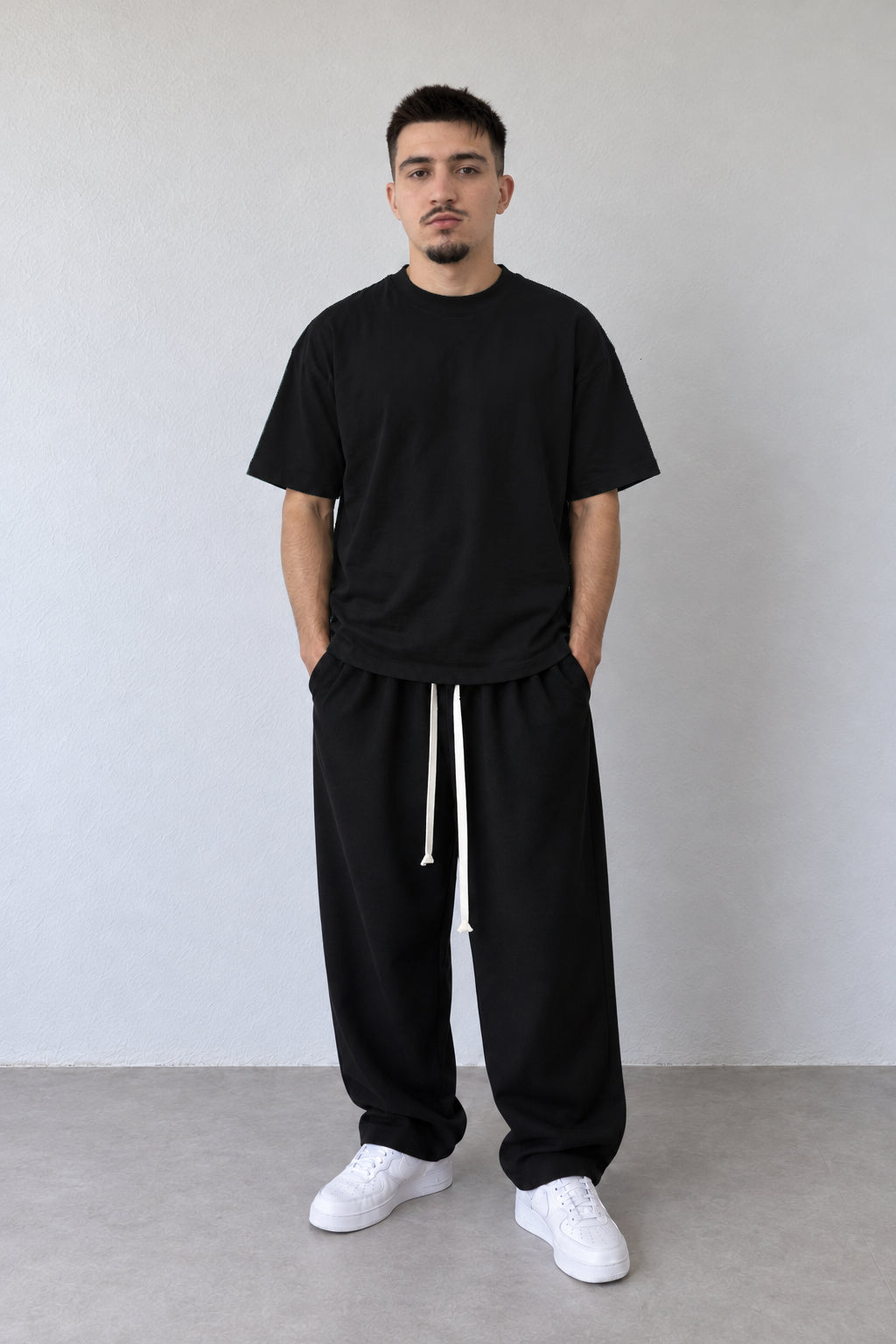 Tricou negru L815002 din bumbac pentru bărbați, cu mâneci scurte și linie lejeră, purtat cu pantaloni largi negri.